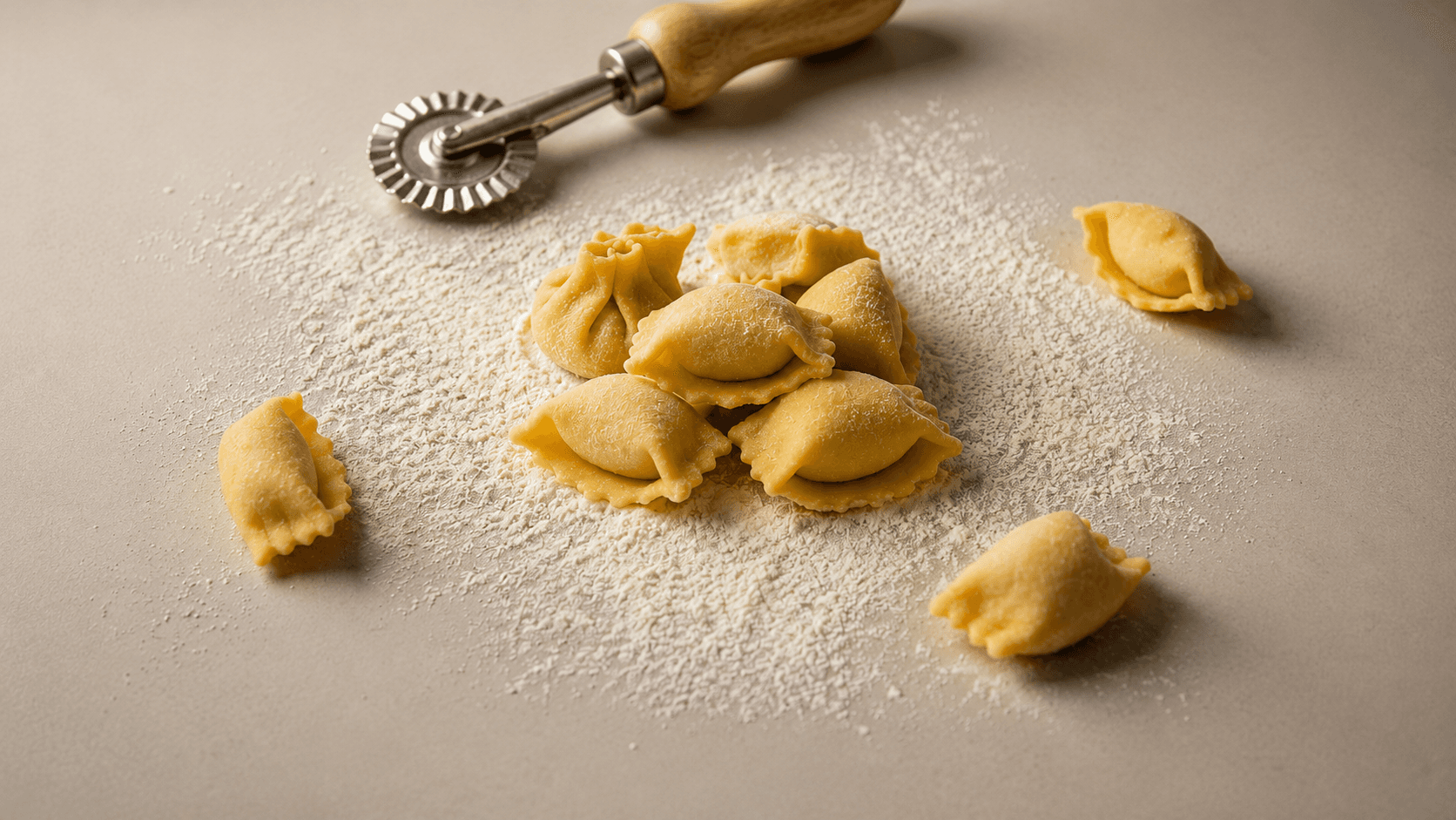 A small cluster of Ravioli Plin, pinched and folded, on a floured surface with a fluted pastry wheel behind them.